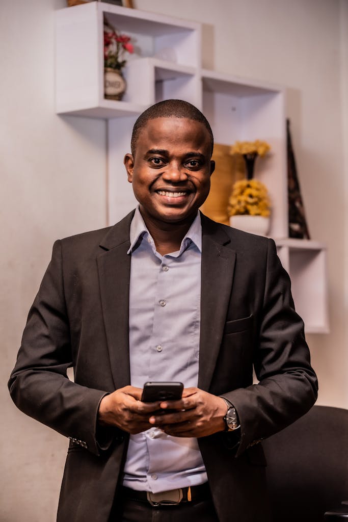 African American businessman in a suit smiling with a smartphone in an office setting.
